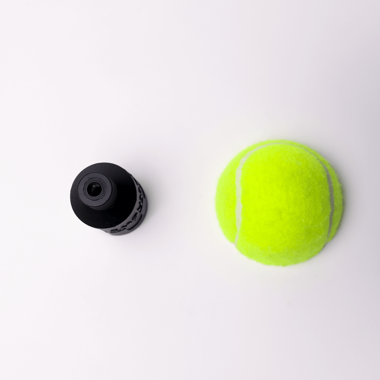 Black rigging accessory next to a bright yellow tennis ball on a white background.