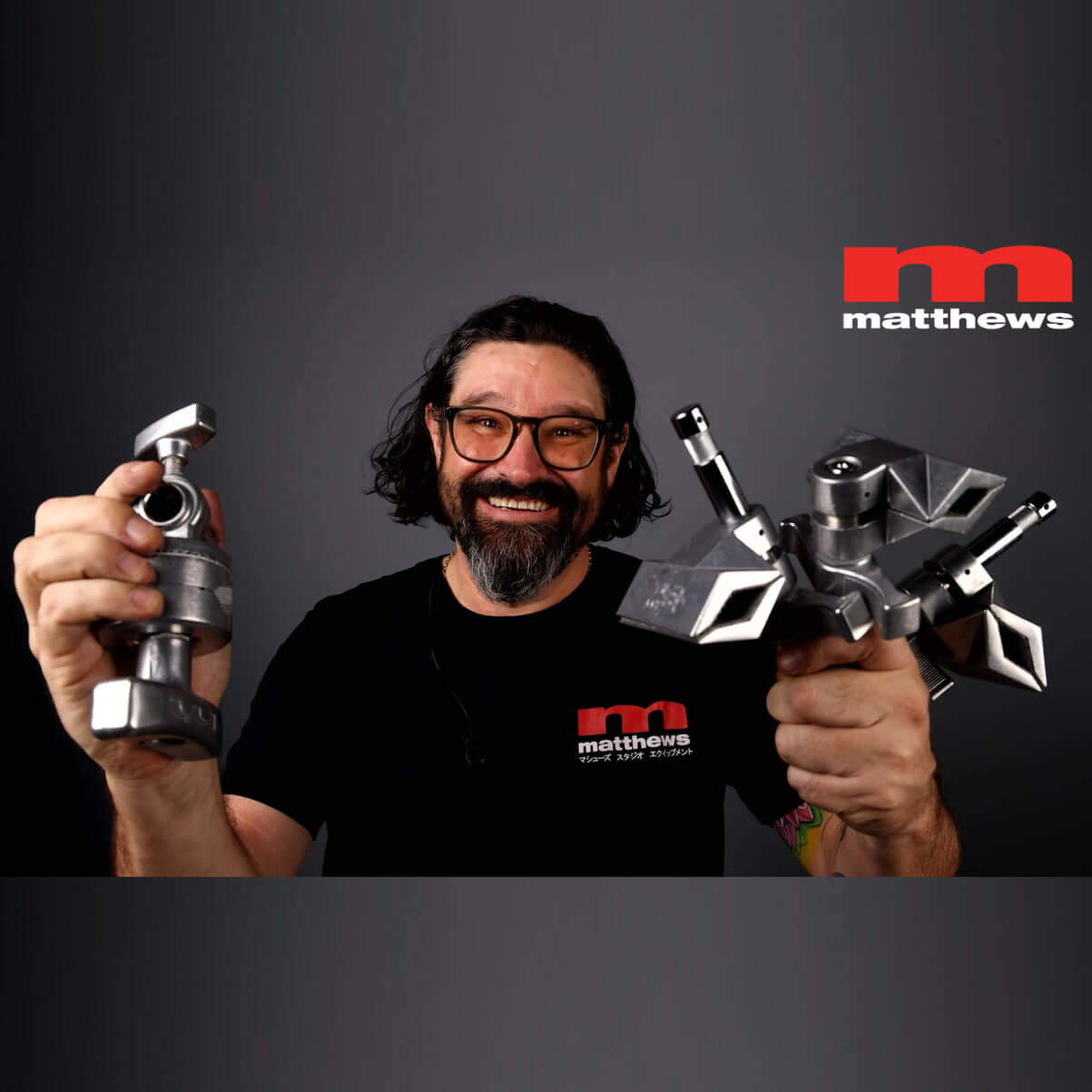 Smiling man holding Matthellini Mounting Kit components, showcasing versatile clamping solutions for photographers.