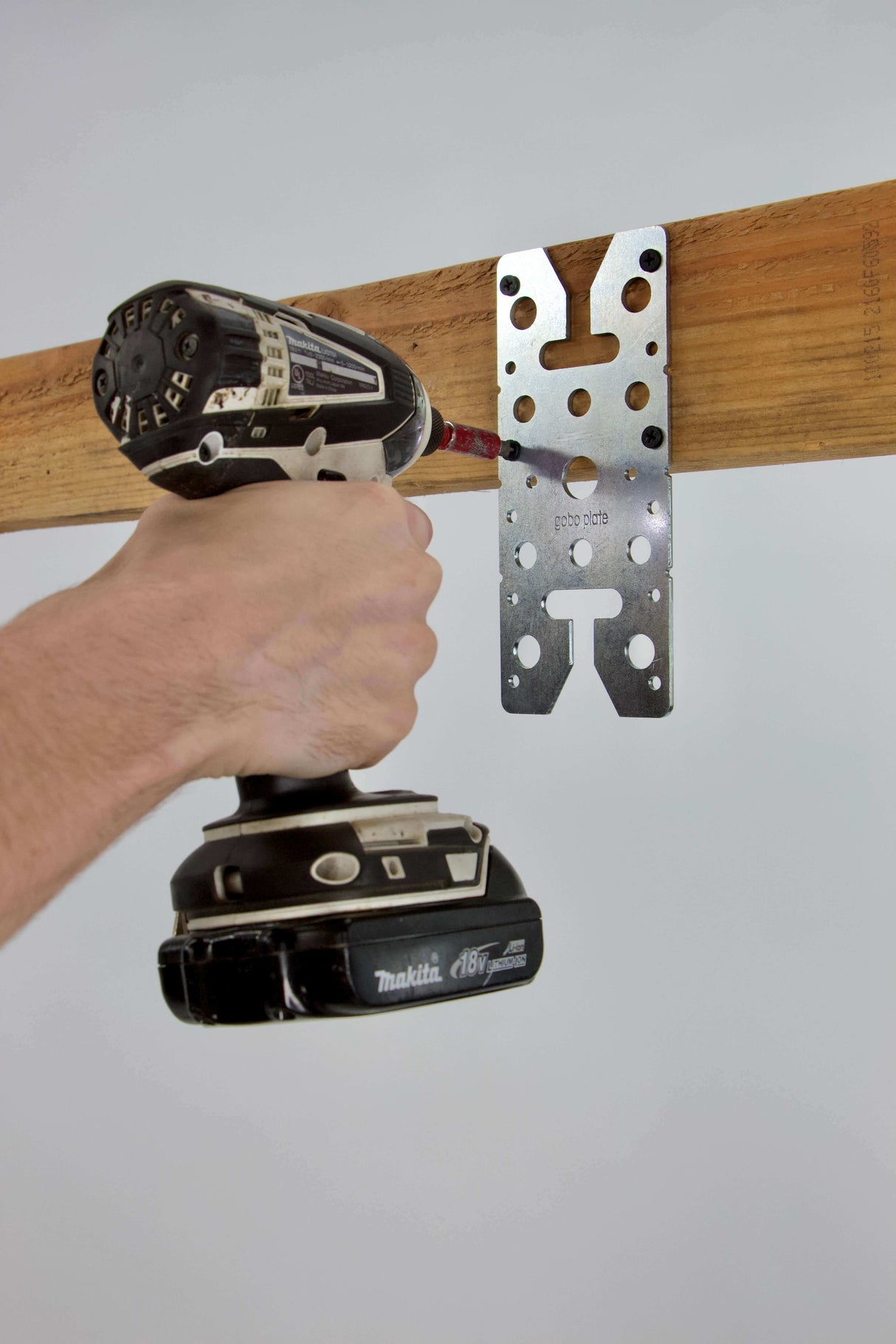 Hand using a drill to attach a Gobo Plate mounting adapter to a wooden beam for versatile equipment compatibility.