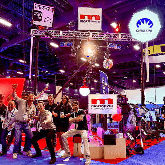 Team celebrating at a trade show booth featuring Matthews Studio Equipment and truss setup.