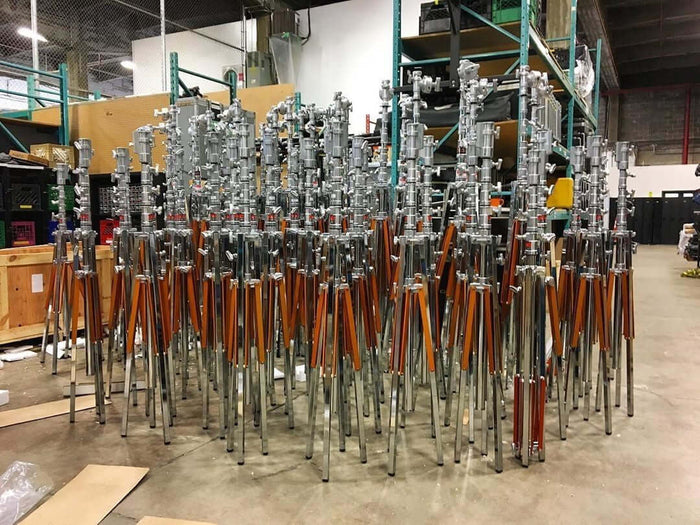 Multiple Mombo Combo stands with adjustable arms and metal bases stored in a warehouse setting.