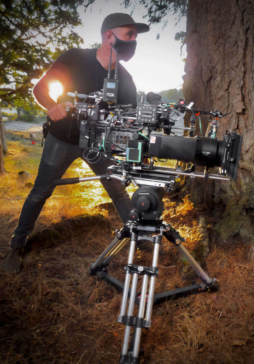 Cinematographer operating advanced camera equipment on a tripod in a natural outdoor setting.