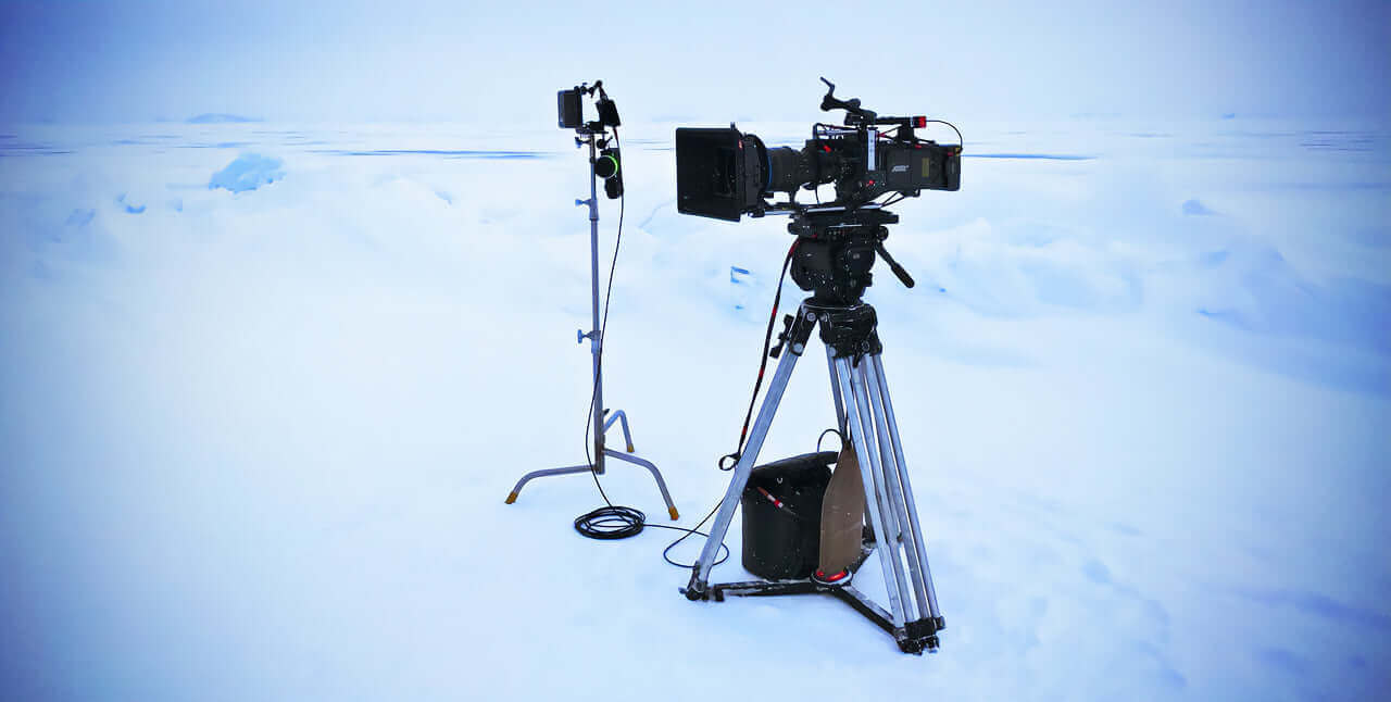 Camera setup on a snowy landscape, featuring tripods and equipment for filming in cold conditions.